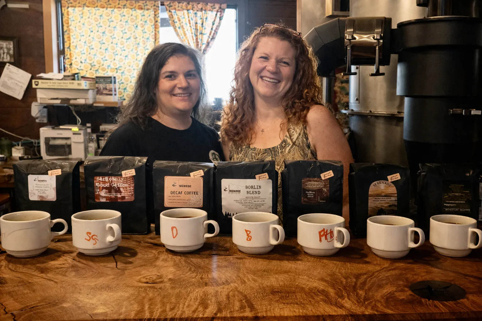 Heather Fulcher and Jody Fulcher Dennett, the sisters who own Monroe Coffee Co., standing behind the bar with bags of freshly roasted beans and cupping cups